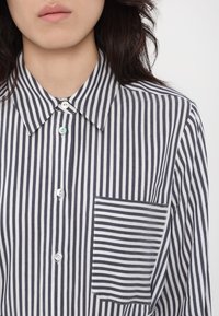 Camicia a righe bianco e blu navy con colletto a punta, dotata di taschino con righe orizzontali, realizzata in tessuto leggero.