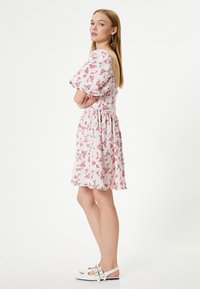 Bloemenjurk met korte pofmouwen, lichtroze stof en een cinched taille. Heeft een open rug en een bloemenpatroon. Gemaakt met witte schoenen.