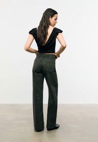 Top nero drappeggiato con profondo scollo sulla schiena, abbinato a jeans verde oliva a vita alta e a gamba dritta con due tasche posteriori.