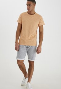 T-shirt en coton orange clair avec col rond, associé à un short en polaire gris avec des revers, complété par des baskets blanches.