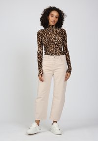 Langärmliges, figurbetontes Oberteil mit Leopardenmuster in Braun und Schwarz; hochgeschnittene, hellbeige Cordhosen; kombiniert mit weißen Sneakern.