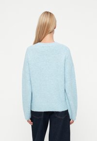 Jasnoniebieski, oversize sweter o miękkiej, puszystej teksturze. Posiada okrągły dekolt, obniżone ramiona oraz ribbowany dół. Noszony z ciemnymi dżinsami.