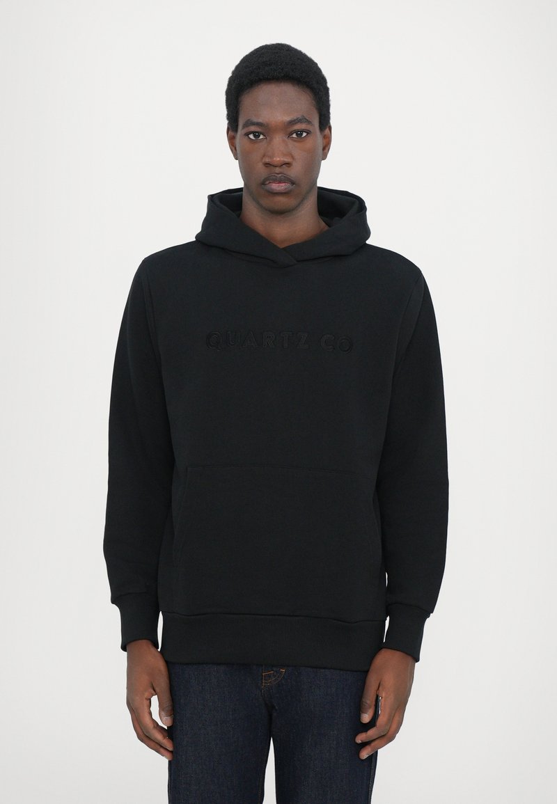 Black hoodie made of soft fabric, featuring a front kangaroo pocket and embossed "QUARTZ CO" logo on the chest, with ribbed hem and cuffs.
