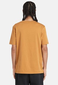 T-shirt a maniche corte e colletto tondo in cotone giallo senape, con una vestibilità rilassata e una piccola etichetta del brand sul lato sinistro in basso.
