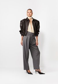 Jachetă bomber neagră din piele, pantaloni gri plisati, top crem cu cravată la gât și pantofi negri cu vârf ascuțit. Cercei mari aurii.