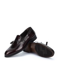 Mocasines de cuero burdeos oscuros con un acabado suave, detalle de borlas y suela de goma texturizada. Presenta un diseño clásico de deslizamiento.