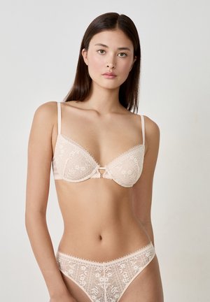Reggiseno in pizzo e perizoma coordinato in rosa chiaro. Il reggiseno presenta coppe imbottite, design floreali e un fiocco centrale. Tessuto morbido e testurizzato in tutto.