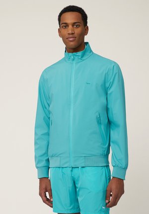 Lichtgewicht turquoise jasje met een rechtopstaande kraag, voorrits en elastische manchetten. Voorzien van zijrits zakken en een subtiele logodetail.