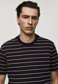 Mörkblå t-shirt med korta ärmar och tunna, kontrasterande beige horisontella ränder, med rundad halsringning och en mjuk, slät textur.