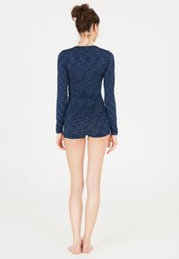 Marineblå langærmet bodysuit med en tekstureret overflade og tætsiddende design, parret med matchende shorts. Glat stof, minimalistisk stil.