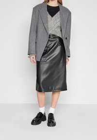 Szary, oversize marynarka, strukturalny szary sweter z dzianiny, czarna, midi spódnica z materiału przypominającego skórę oraz czarne lakierowane buty na sznurowadła z grubą podeszwą.