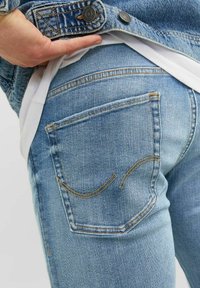 Jeans de mezclilla de color azul claro con un diseño ajustado. Las características notables incluyen bolsillos traseros cosidos con acentos curvados y una textura sutil.