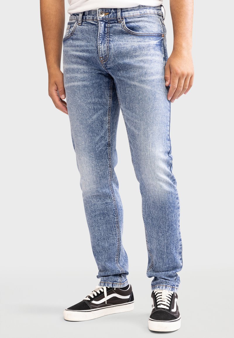 Lyseblå denimjeans med en falmet finish, der har fem lommer, en lynlås og kontraststing. Parret med sorte sneakers.