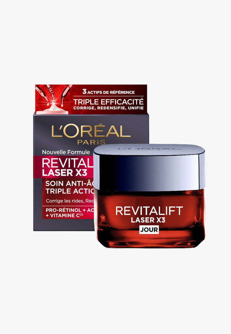 Bocal en verre rouge avec un couvercle en métal argenté étiqueté "Revitalift Laser X3". Boîte noire à l'arrière avec des accents rouges et un texte doré, indiquant les bienfaits anti-âge.