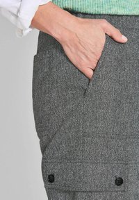 Grau strukturierte Hose mit Fischgrätenmuster, die über eine Seitentasche und schwarze Knopfakzente verfügt. Hand liegt in der Tasche.