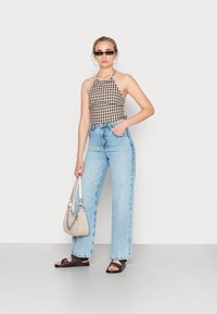 Top de halter xadrez castanho e branco, jeans de cintura alta azul claro, sandálias pretas de deslizar e uma bolsa cinza com um acento de corrente prateada.
