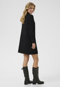 Black long-sleeve dress featuring a relaxed fit and ribbed hem, paired with knee-high black leather boots with buckle accents.