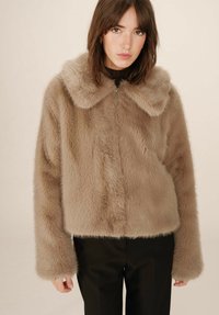 Giacca in finta pelliccia marrone con colletto ampio, design cropped e maniche lunghe. Presenta una zip frontale e una superficie morbida e texturizzata.