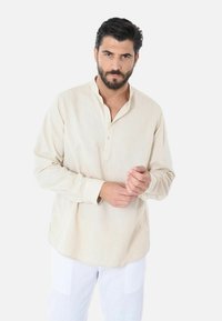 Camicia beige a maniche lunghe con colletto henley abbottonato, realizzata in tessuto leggero, con una vestibilità comoda e una texture sottile.