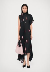 Long black dress with floral pattern in shades of burgundy, featuring a high neckline and asymmetrical hem. Paired with a light pink bag.