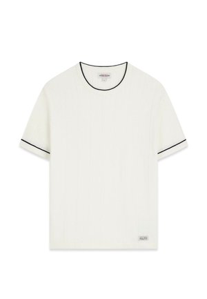 Baltas trumpomis rankovėmis marškinėlis su juoda apdaila ant apykaklės ir rankovių kraštų, turi mažą etiketę apatiniame kampe.