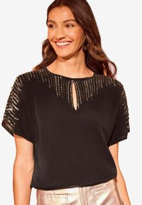 Blusa nera a maniche corte con scollatura a chiave e decorazioni in paillettes lungo le spalle. Tessuto morbido e leggero.