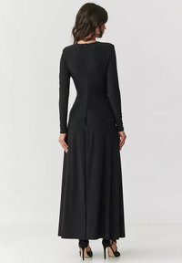 Czarna sukienka z długim rękawem, dopasowaną górą i zwiewnym dołem. Posiada okrągły dekolt i zamek błyskawiczny z tyłu. Nosi się z czarnymi szpilkami.