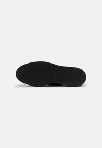 Semelle de chaussure noire avec une surface lisse et plate et de légères nervures. Caractérisée par un logo embossé sur le côté. Design minimaliste sans motifs.