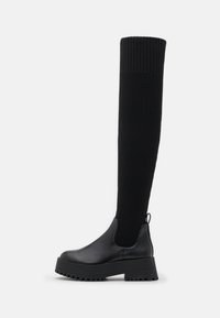 Knähöga svarta stövlar med ribbad tygövre och slätt läderunderdel. Chunky plattformsula med texturerad detalj. Dragflik baktill.