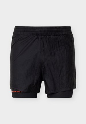 Melnas vīriešu sporta šortus ar iebūvētiem kompresijas šortiem un elastīgu jostu, attēloti uz vienkārša fona.