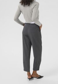Pantalones grises, ajustados y de pierna recta, con bolsillos traseros y una textura suave, combinados con un suéter corto gris claro y tacones negros.