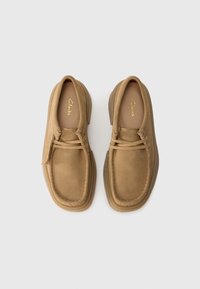 Paire de chaussures décontractées Clarks en daim beige à lacets vue de dessus sur un fond clair uni.