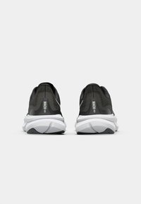 Des chaussures de course noires avec une tige en mesh texturé, une intermédiaire blanche et une semelle extérieure en caoutchouc noir. Présente le logo "MACH" sur le talon.