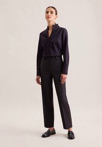 Blusa con colletto navy, abbottonata, abbinata a pantaloni neri a vita alta, con gambe dritte, indossata con mocassini neri lucidi.