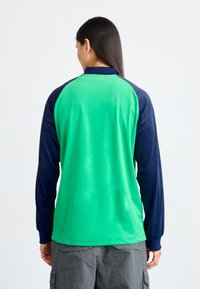 Majica s dugim rukavima u zelenoj boji tijela i mornarsko plavim raglan rukavima, izrađena od glatkog materijala s okruglim izrezom i jednostavnim dizajnom.