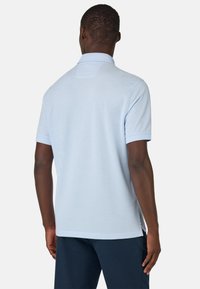 Polo de color azul claro hecho de tela suave, con cuello tipo solapa, mangas cortas y aberturas laterales para mayor libertad de movimiento.