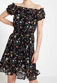 Svart blommig off-shoulder klänning med korta volangärmar, med en cinchad midja och en vid nederdel med volangdetaljer.