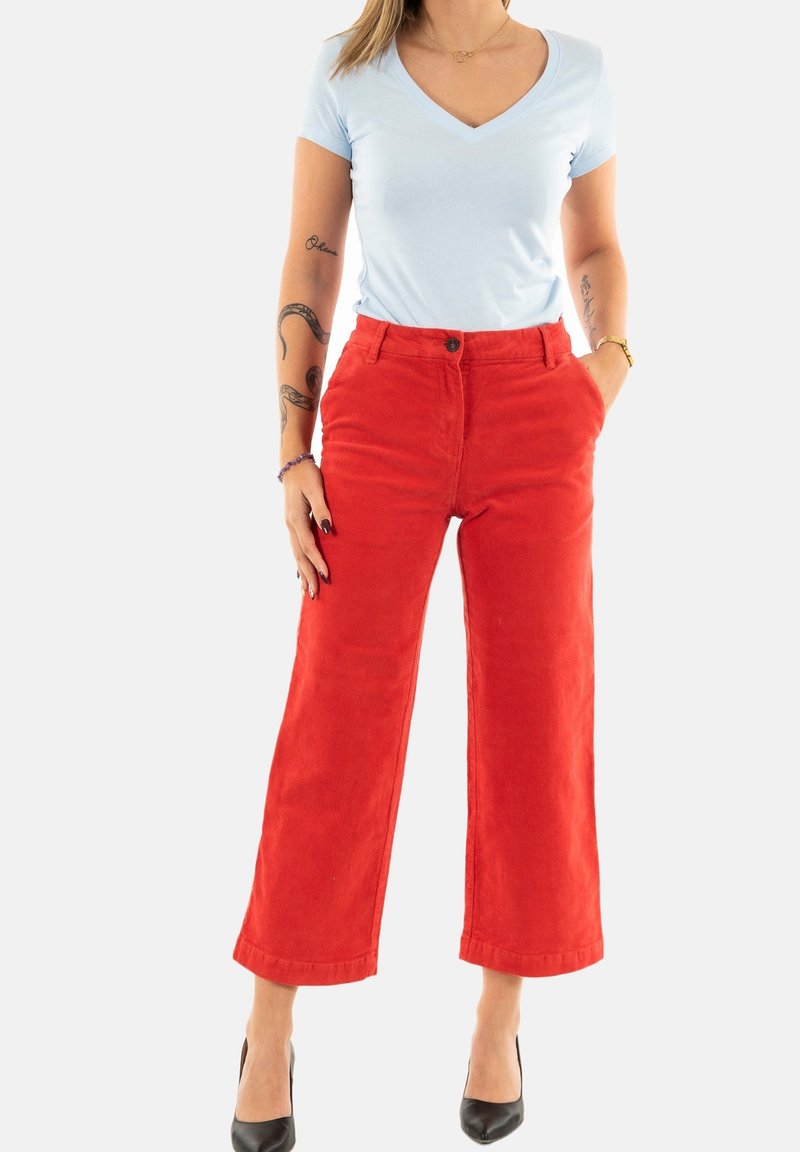Pantalons en velours côtelé rouge à jambes larges avec une fermeture à boutons et des poches avant, associés à un t-shirt à col en v bleu clair et des talons noirs.