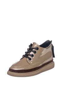 Chaussure beige brillante à la cheville avec lacets noirs, garniture en daim marron, semelle beige texturée et languette zippée arrière sur fond blanc.