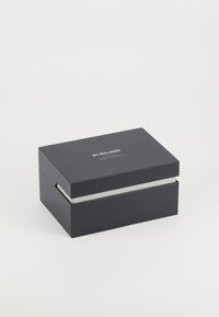 Boîte rectangulaire noire en carton texturé avec un intérieur lisse et blanc. Présente un logo simple sur le dessus et un mécanisme d'ouverture encastré.