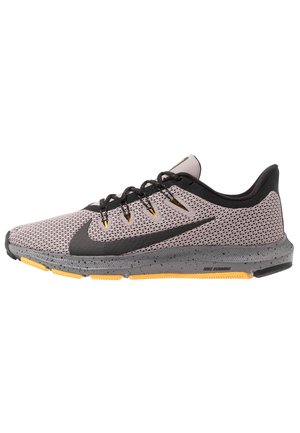 Lysegrå Nike løbesko med sort swoosh, sorte snørebånd med gule accenter, grå plettet sål og gule detaljer på ydersålen.