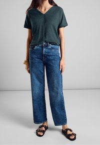 Haut court texturé vert à col en V, associé à un jean bleu à jambes larges et des sandales noires avec des accents de chaîne décoratifs.