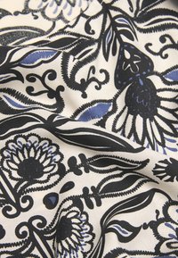 Blomstermønstrede stof med sorte og blå motiver på en cremefarvet baggrund, med detaljeret design og glat tekstur.