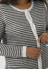 Cardigan rayé noir et blanc, avec col rond, fermeture à boutons, et poignets et ourlet côtelés. Matière en maille douce et texturée.