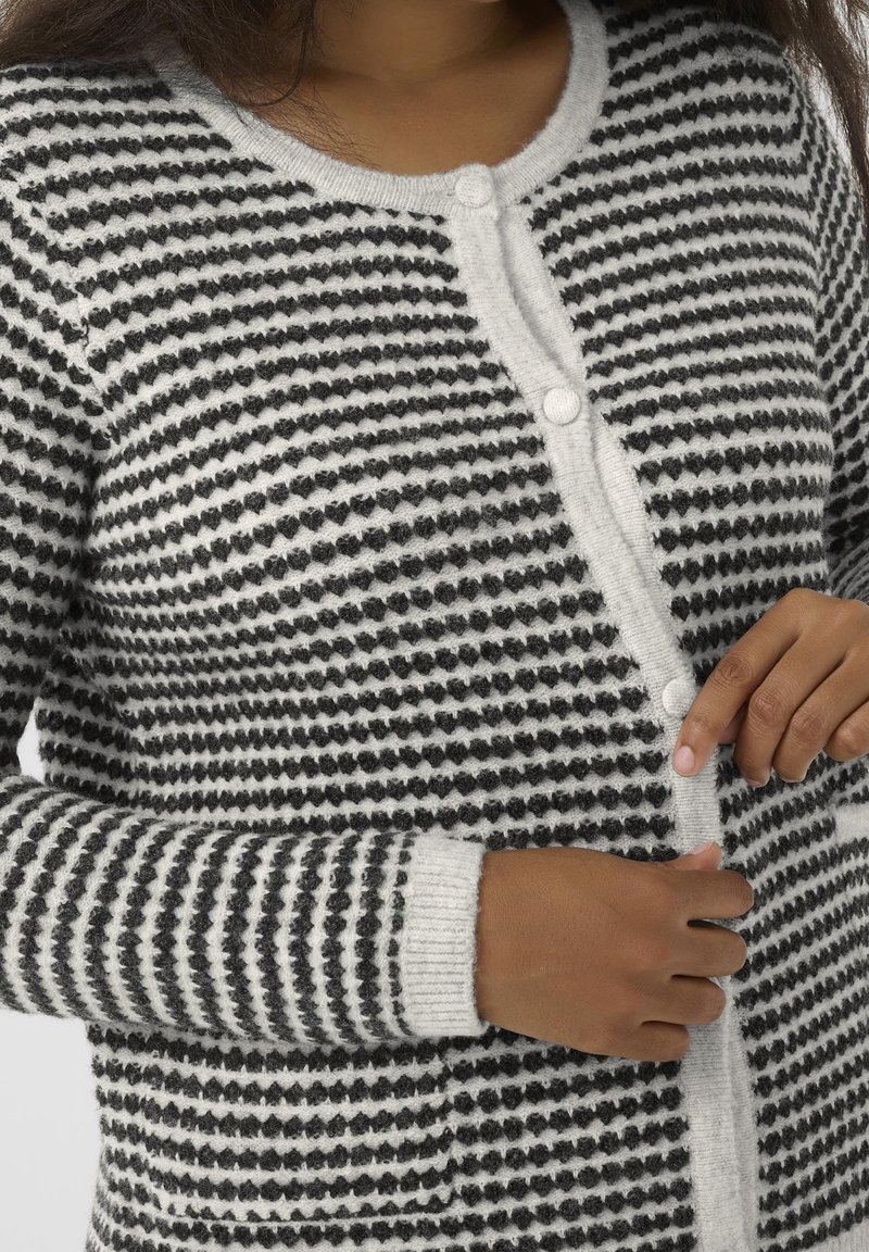 Cardigan rayé noir et blanc, avec col rond, fermeture à boutons, et poignets et ourlet côtelés. Matière en maille douce et texturée.