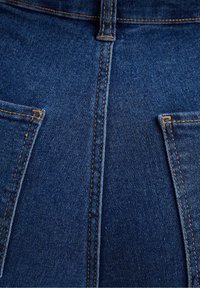 Tela de denim azul oscuro con un primer plano de la textura, las costuras y los detalles de los bolsillos con hilo naranja-marrón en contraste.