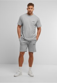 Graues Baumwoll-T-Shirt mit Rundhalsausschnitt und Logo auf der Brust, kombiniert mit passenden grauen Shorts mit seitlichen Taschen. Getragen mit weißen Sneakers.