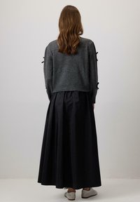 Grijze gebreide trui met lange mouwen, voorzien van zwarte lintaccenten. Gecombineerd met een zwarte, vloeiende maxi-rokken en lichtgrijze schoenen.