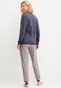 Marineblaues Langarmoberteil kombiniert mit gemusterten Schlafanzughosen in hellen Farben, mit elastischen Bündchen und Bund, glatte Stofftextur.