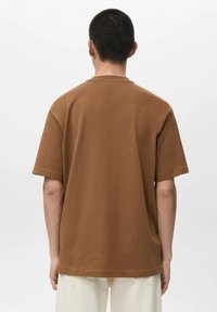 Brązowy bawełniany t-shirt z krótkim rękawem, luźny fason, okrągły dekolt, gładka struktura, jednolity wzór, widoczne przeszycia wzdłuż dolnego brzegu i rękawów.